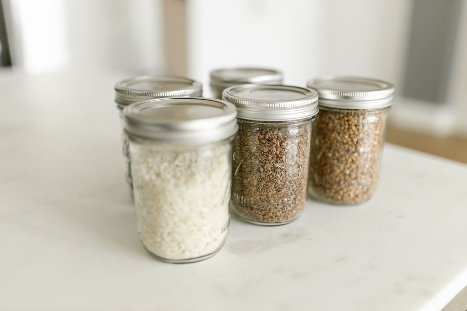 Four glass jars of rice and grains with metal lids on a white counter