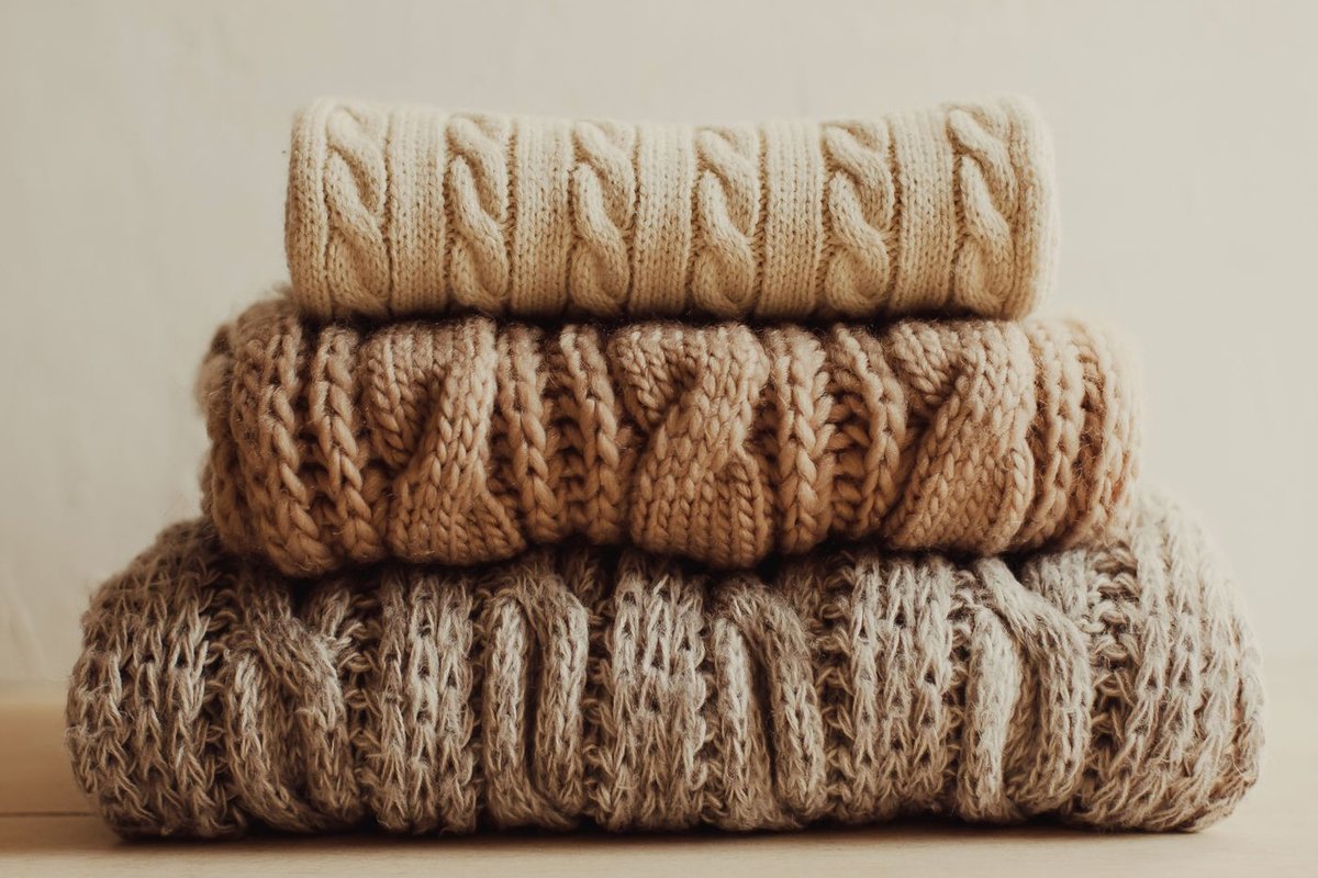 Stack of three folded knit sweaters in cream, tan and oatmeal