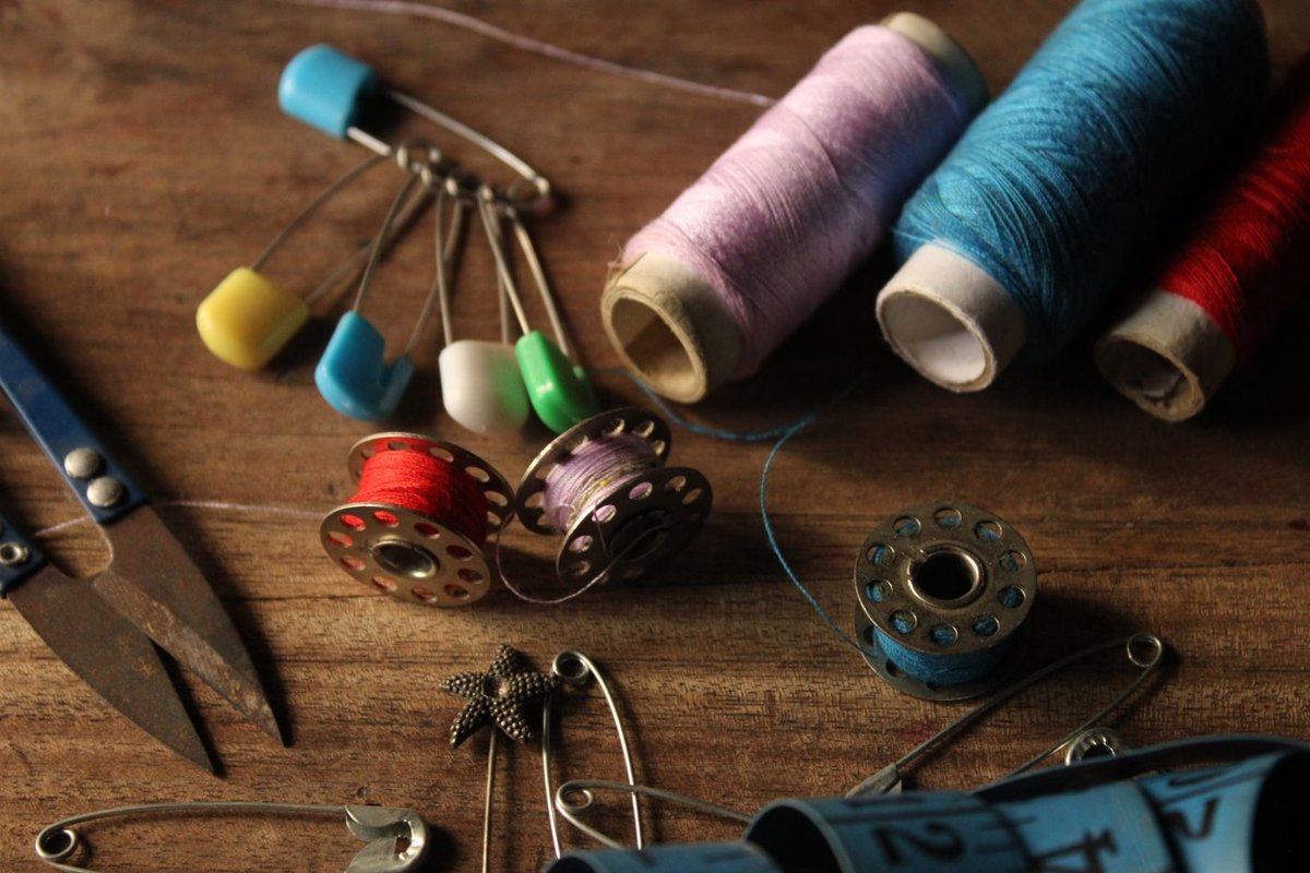 Spools of thread, bobbins, safety pins and small scissors on a wooden table